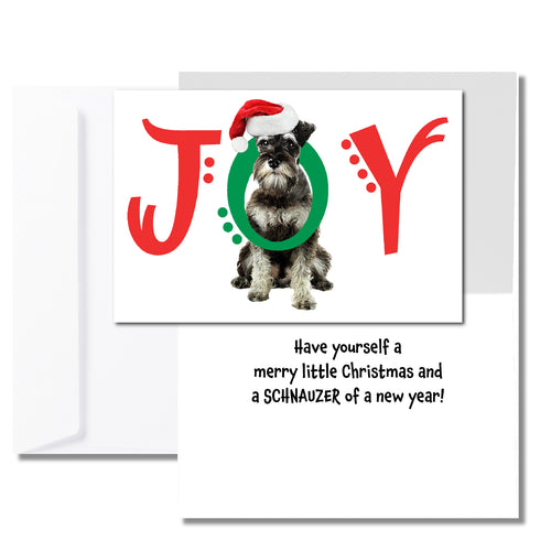 A white Christmas card with a schnauzer dog on the front with the word JOY. The J and Y are red, and the O is green and wrapped around the dog's neck. Inside is a pre-printed message that reads, 